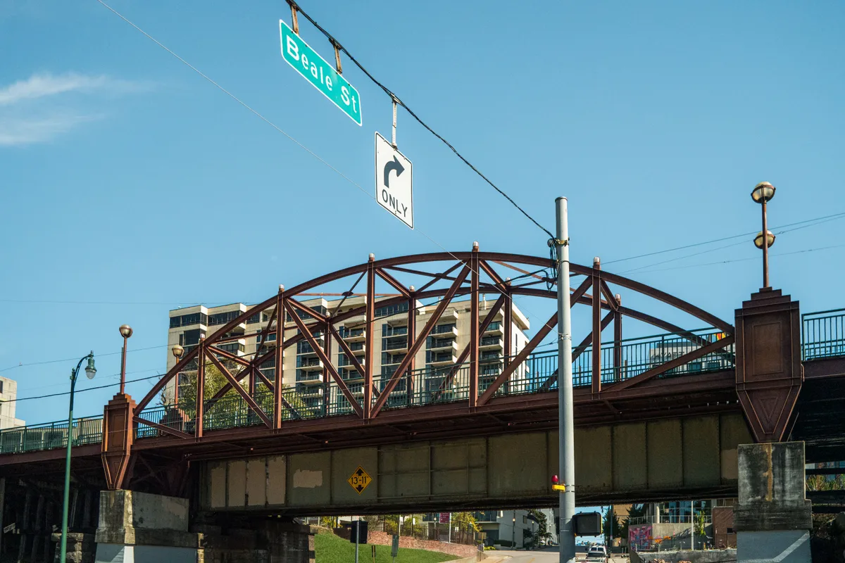 Steel bridge over Beale Street in Memphis with street signs and buildings under blue sky